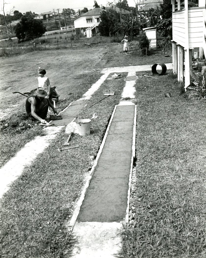 Family Working In Their Backyard - Father Laying Concrete Driveway - Mother Gardening and Daughter Looking On - Darra.