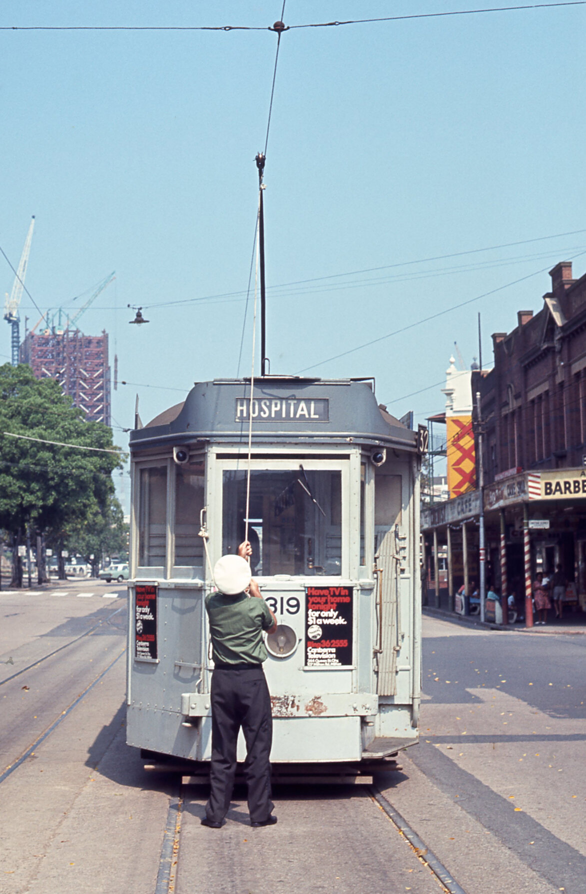 Driver attaching pantograph to wire on tram No. 319 outside Roma Street Station - 1968