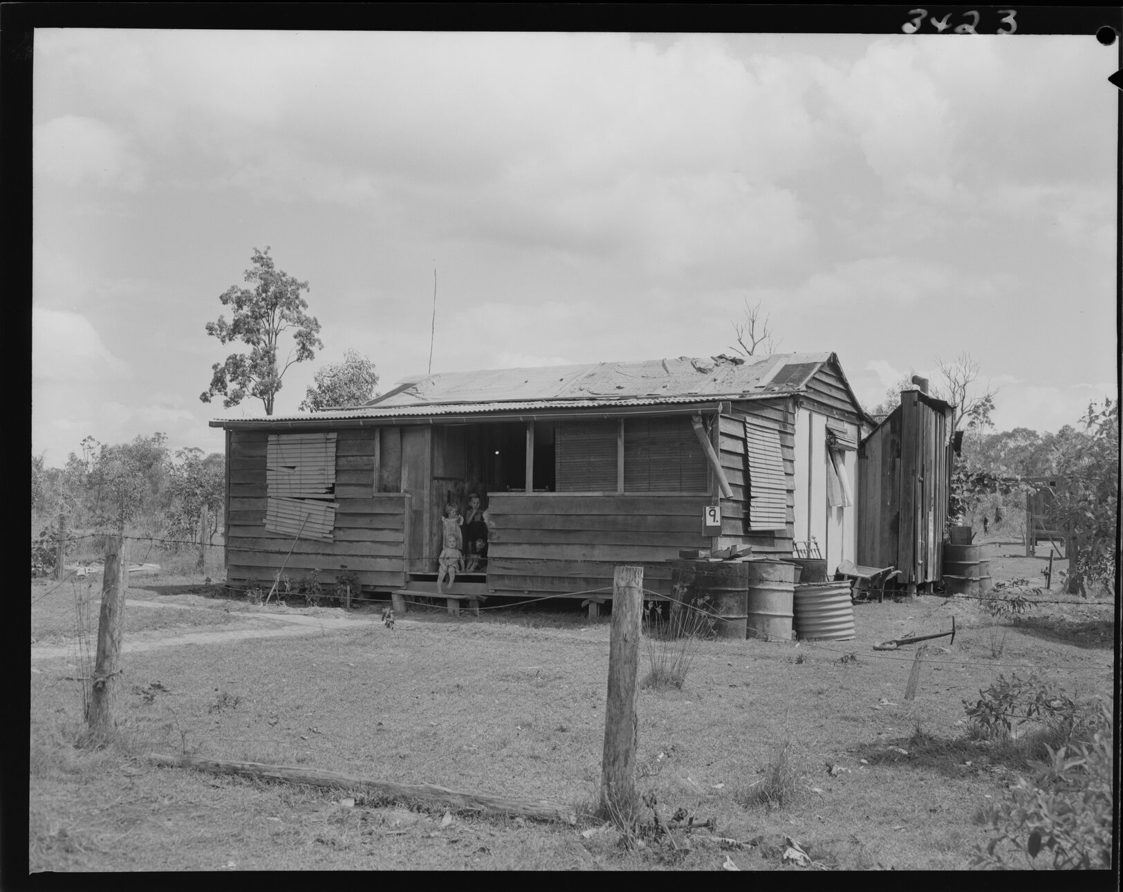 Temporary house labelled 9 in Wacol with barbed wire fence and three children - 1953