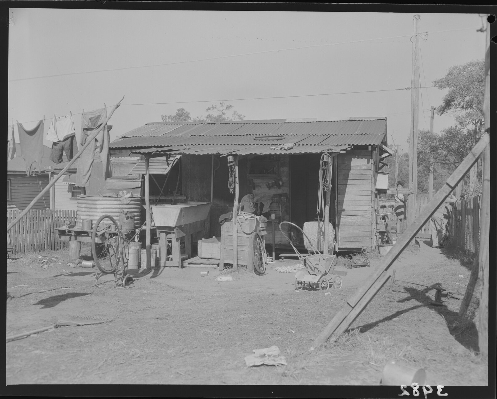 Temporary dwelling with washing line, laundry tub and pram with boy beside, Lota or Wynnum - 1953