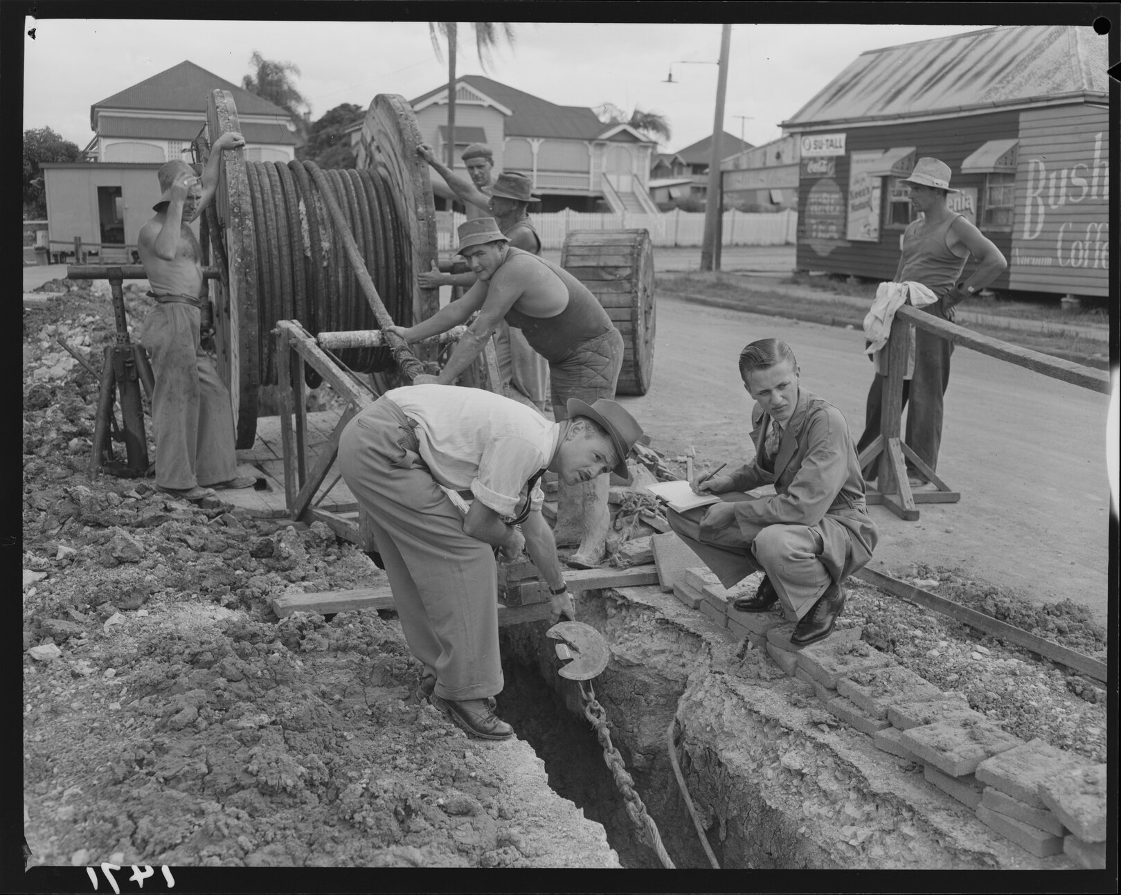 Council workmen laying cable in ditch in street - 1950