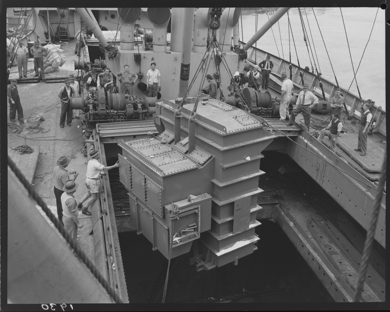 Electrical transformer is unloaded from a ship as crowd watches on Howard Smith Wharves, 1951