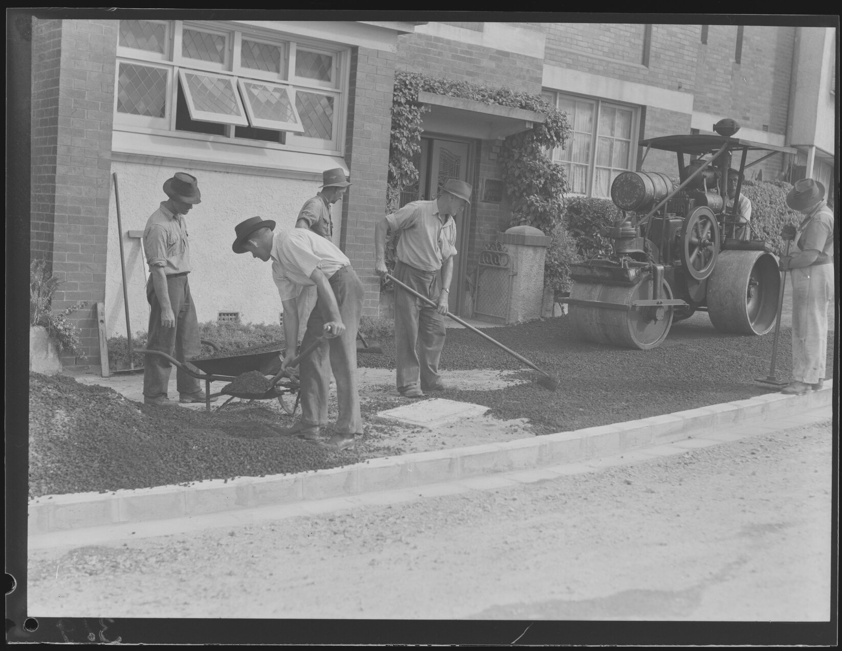 Workers surfacing roads and footpaths with bitumen and steamroller - 1949