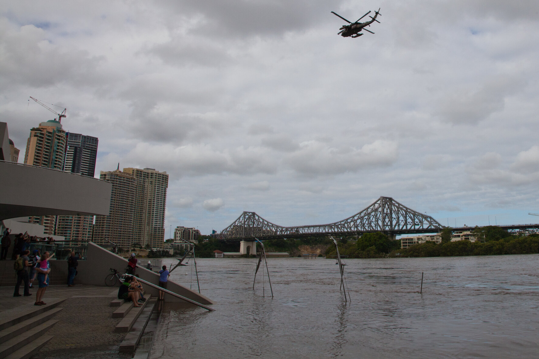 People watch a military helicopter fly over floodwaters near Riverside ferry terminal, looking towards the Story Bridge, Brisbane City - 2011