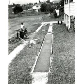 Family Working In Their Backyard - Father Laying Concrete Driveway - Mother Gardening and Daughter Looking On - Darra.