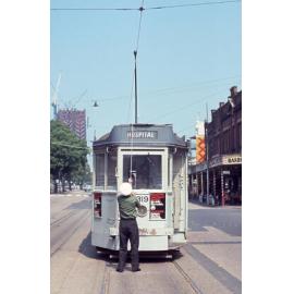 Driver attaching pantograph to wire on tram No. 319 outside Roma Street Station - 1968